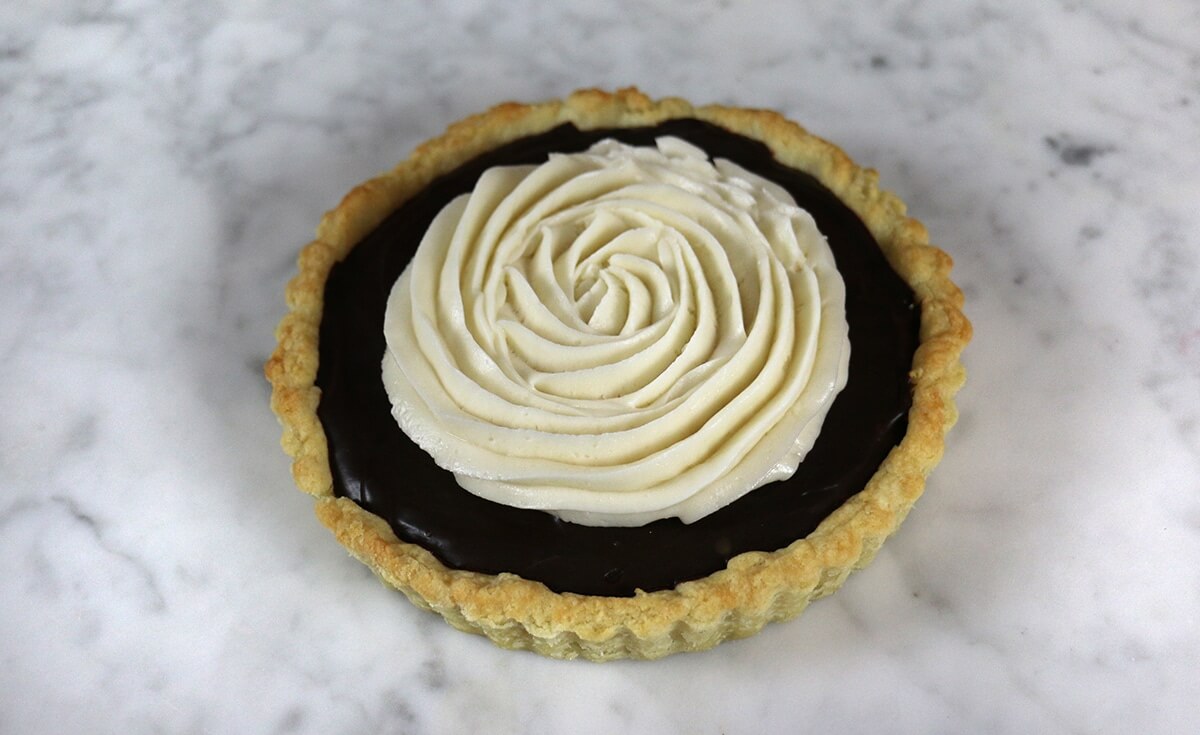 A photo of a chocolate tart topped with a spiral of buttercream.