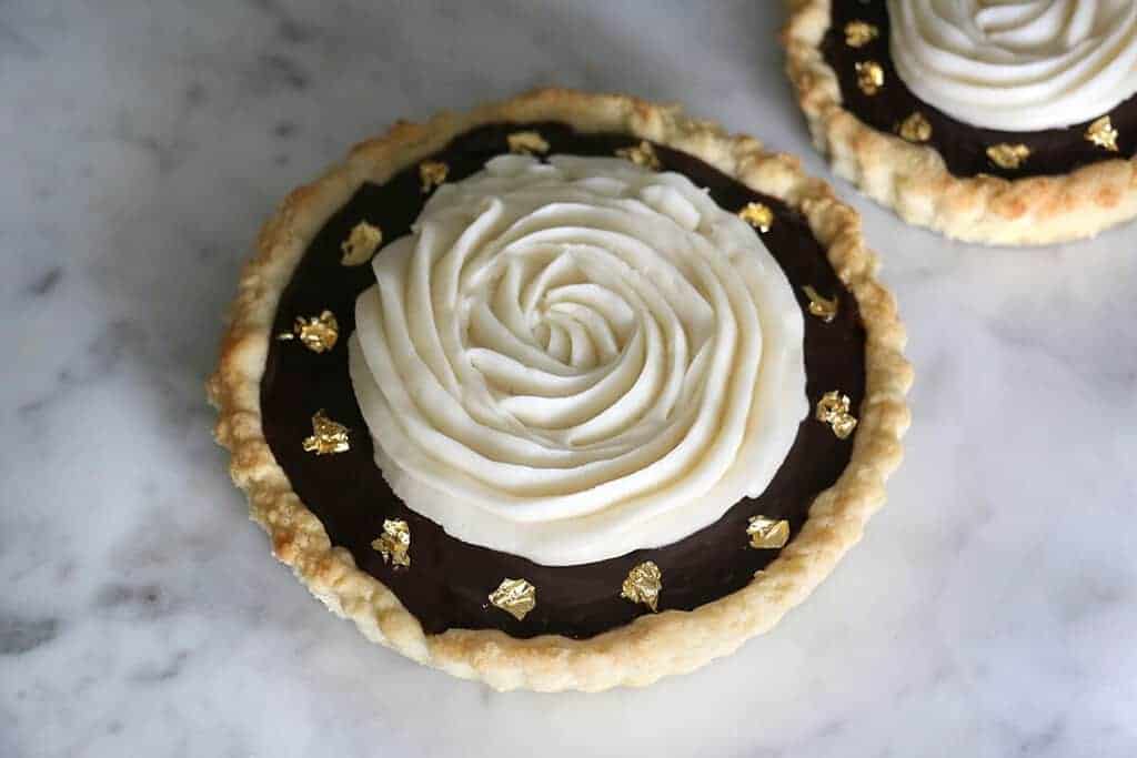 A photo of a chocolate tart topped with a spiral of buttercream and decorated with edible gold leaf.