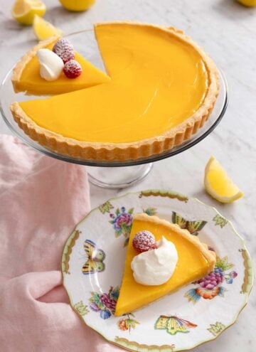 A lemon tart on a cake stand with a slice plated in front.