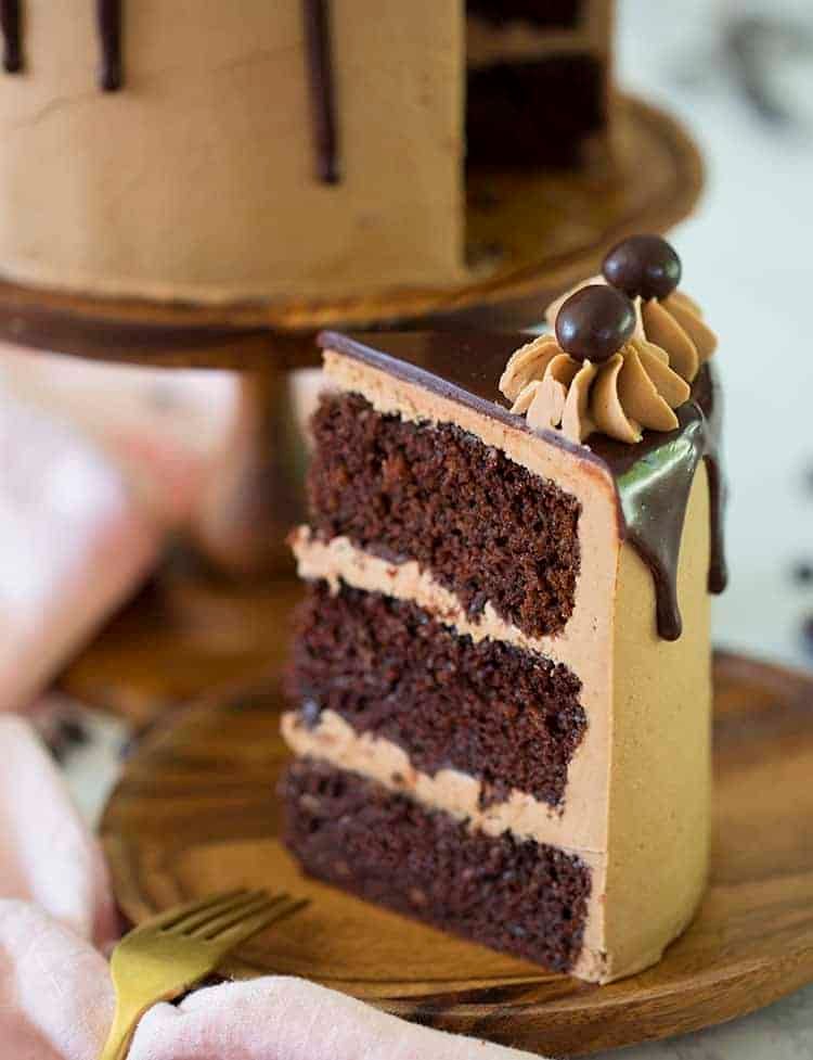 A slice of mocha cake with a ganache drip on a wooden plate
