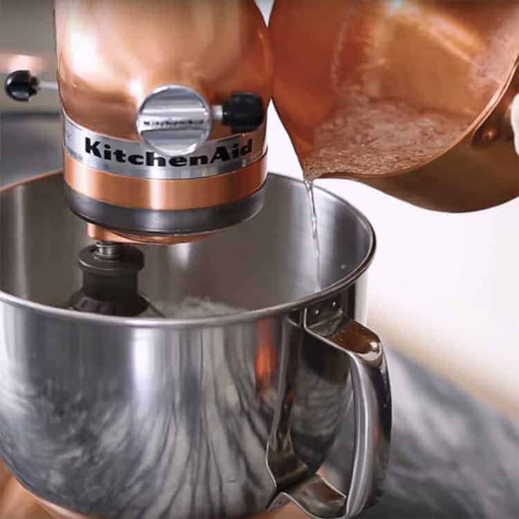 hot sugar being drizzled into a stand mixer filled with meringue