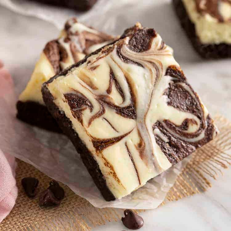 Cheesecake brownies swirled with chocolate on a white marble table.