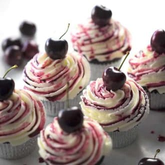 A group of chocolate cherry cupcakes on a white marble table.