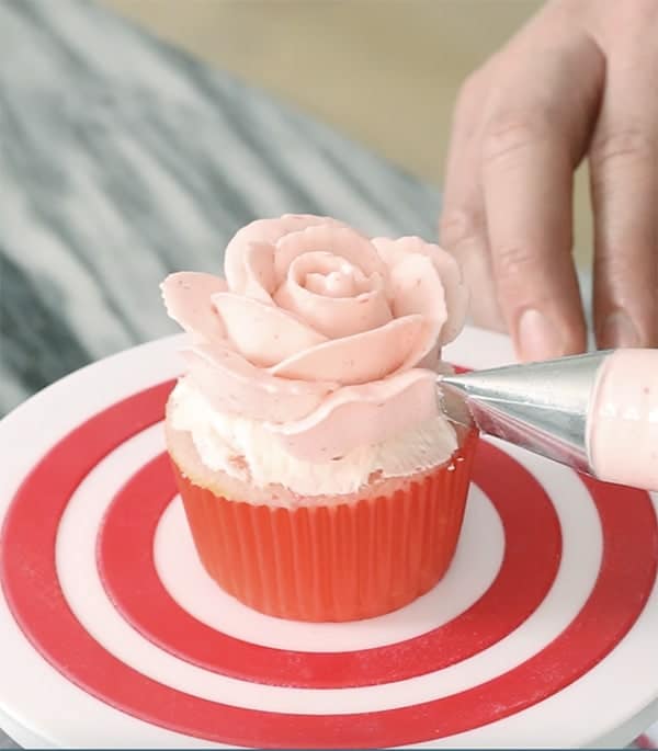 A photo showing a pink buttercream rose being piped onto a pink cupcake.
