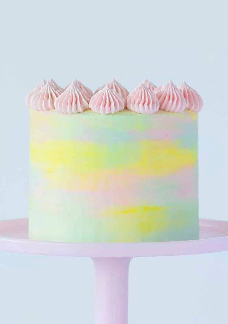 A pastel watercolor cake on a pink cake stand