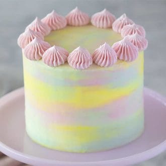 A pastel pink, blue and yellow watercolor cake on a pink cake stand.