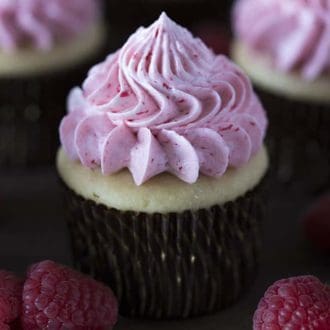A peanut butter and jelly cupcake with raspberries in the foreground.