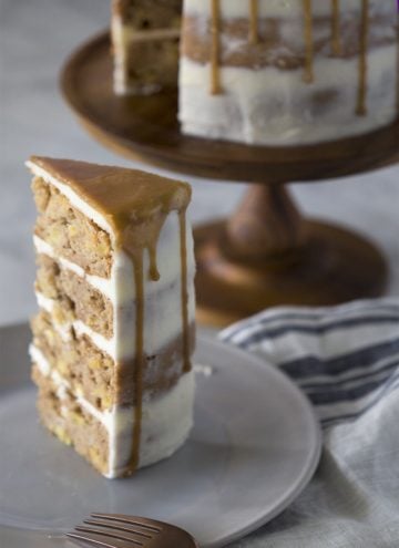 A piece of apple spice cake on a plate with the rest of the cake behind it.