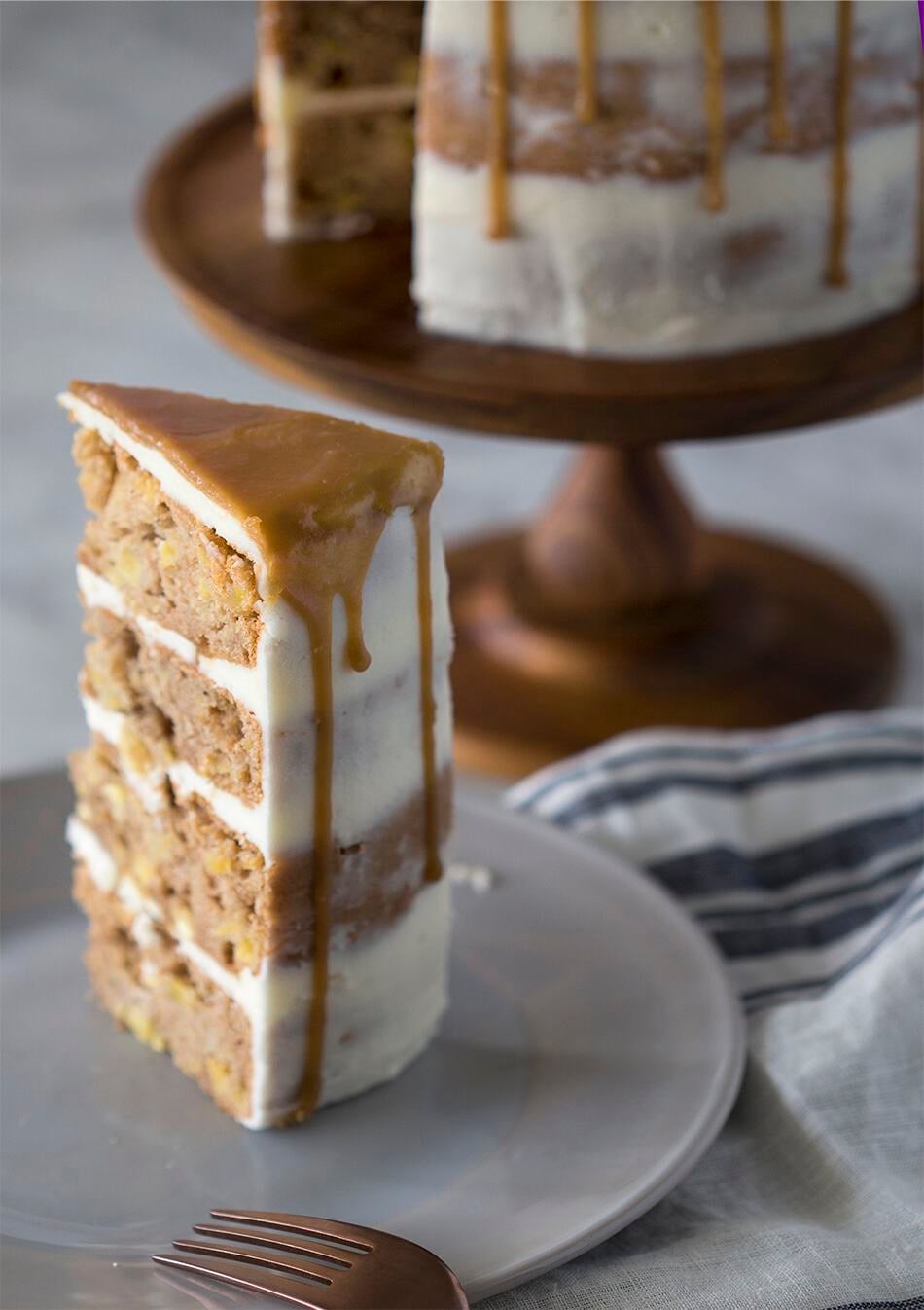 A piece of apple spice cake on a plate with the rest of the cake behind it.