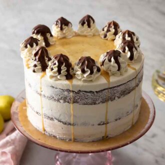 A chocolate pear cake on a cake stand with a pear and plates beside it.