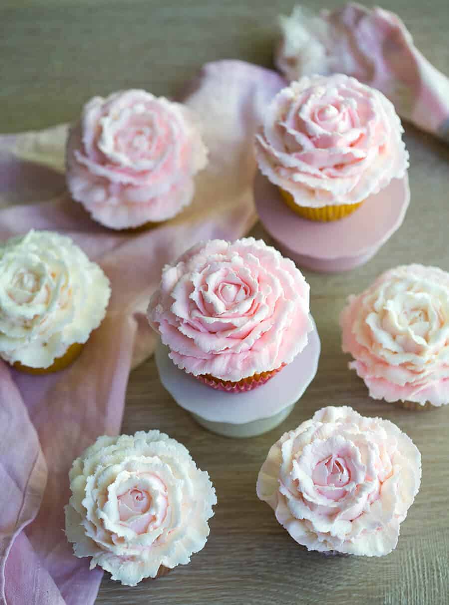 Multiple rose cupcakes with two on mini cupcake stands.