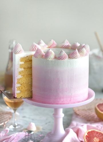 A photo of a champagne grapefruit cake on a pink cake stand with a piece being removed.