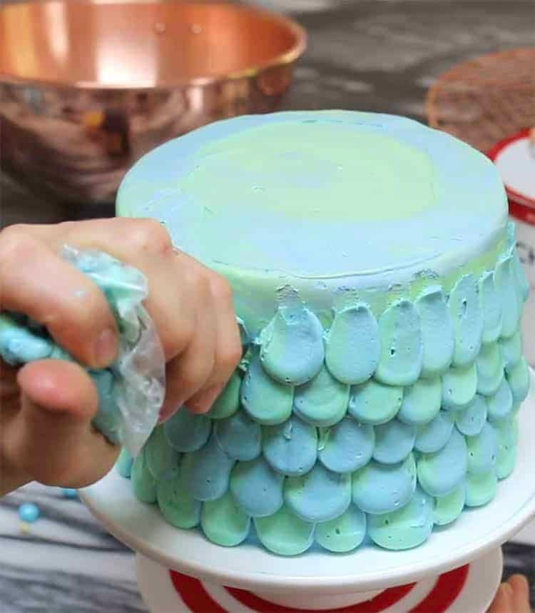 a mermaid cake being piped with light blue buttercream