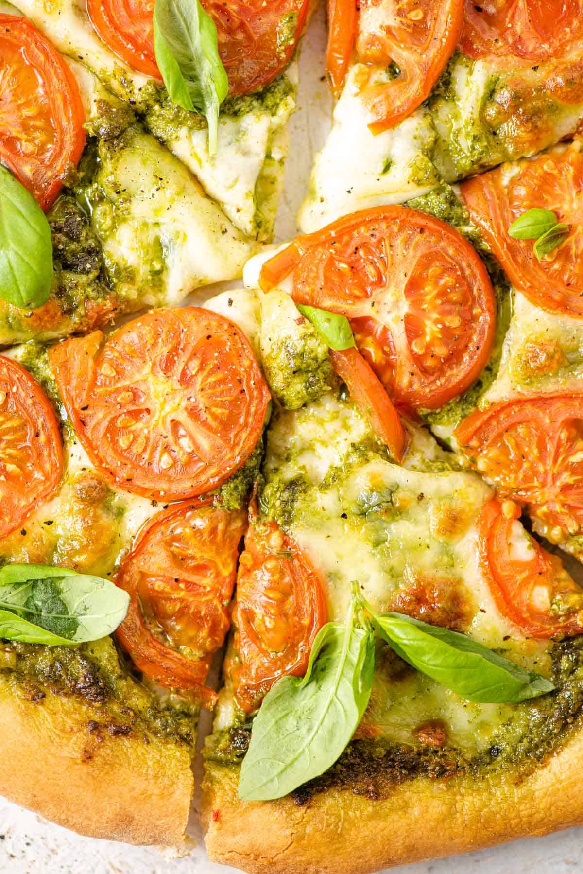 A close up of a pesto pizza topped with mozzarella and sliced tomatoes