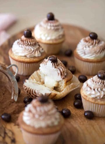 Multiple tiramisu cupcakes with the one in the middle cut in half to show the interior.
