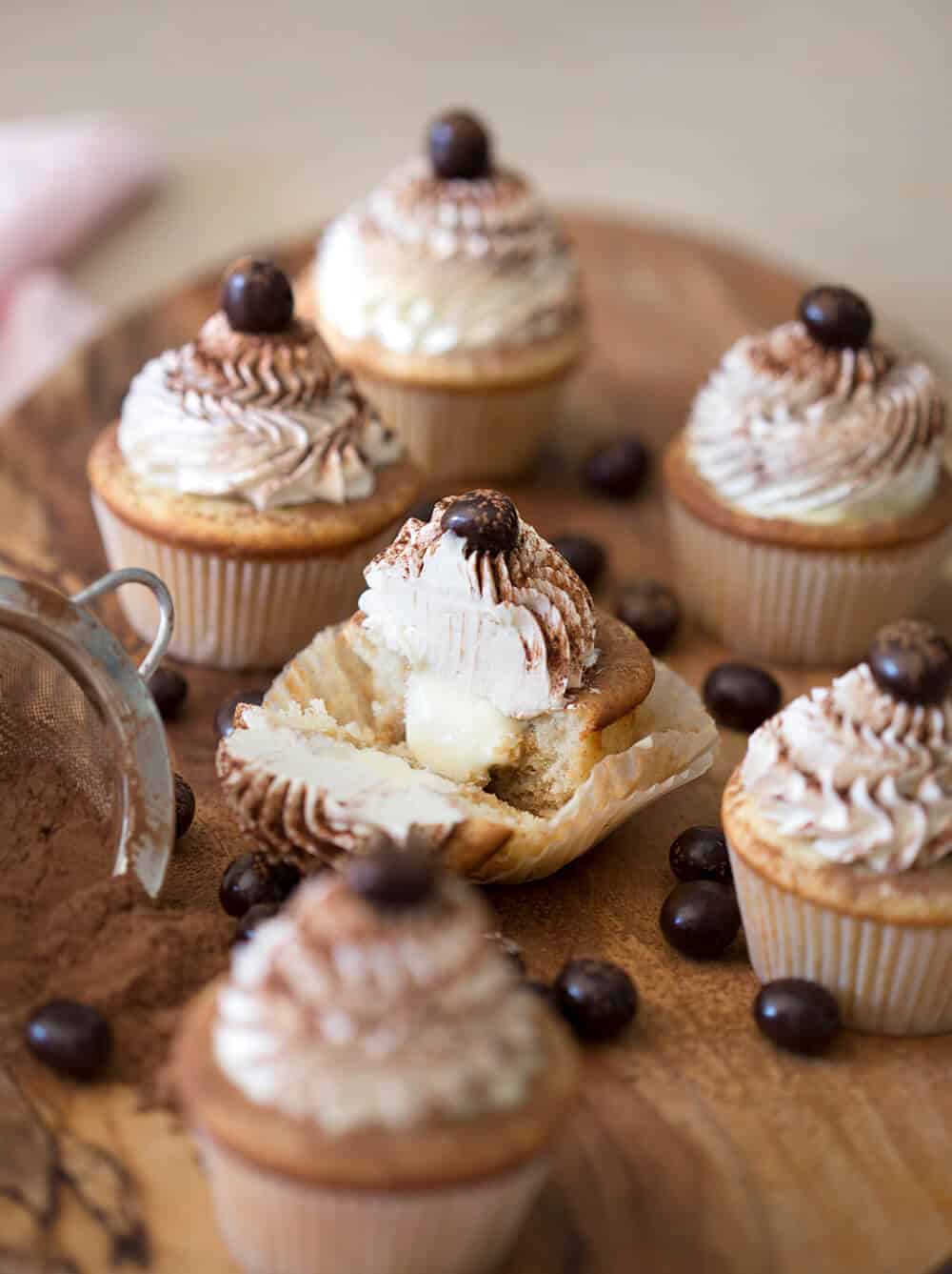 Multiple tiramisu cupcakes with the one in the middle cut in half to show the interior.