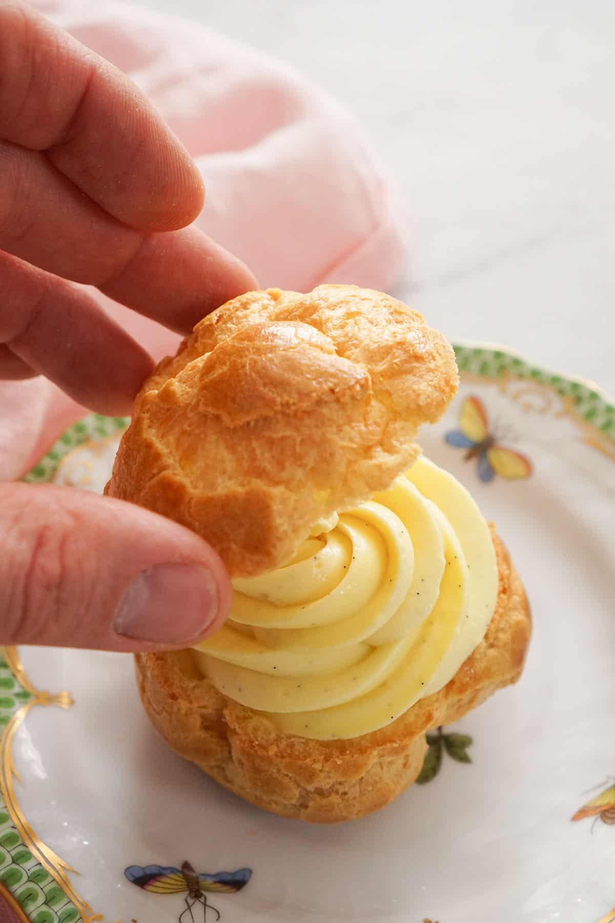 A cream puff getting assembled with piped pastry cream.
