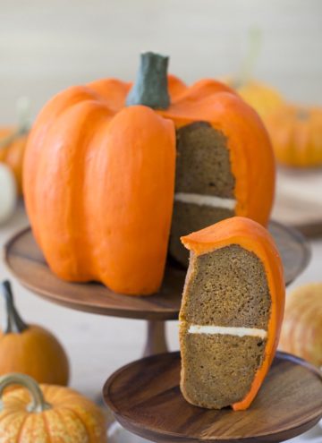 Photo of a large orange pumpkin cake with a piece in the foreground.