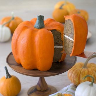 photo of a pumpkin shaped cake on a wooden stand with a piece being removed.
