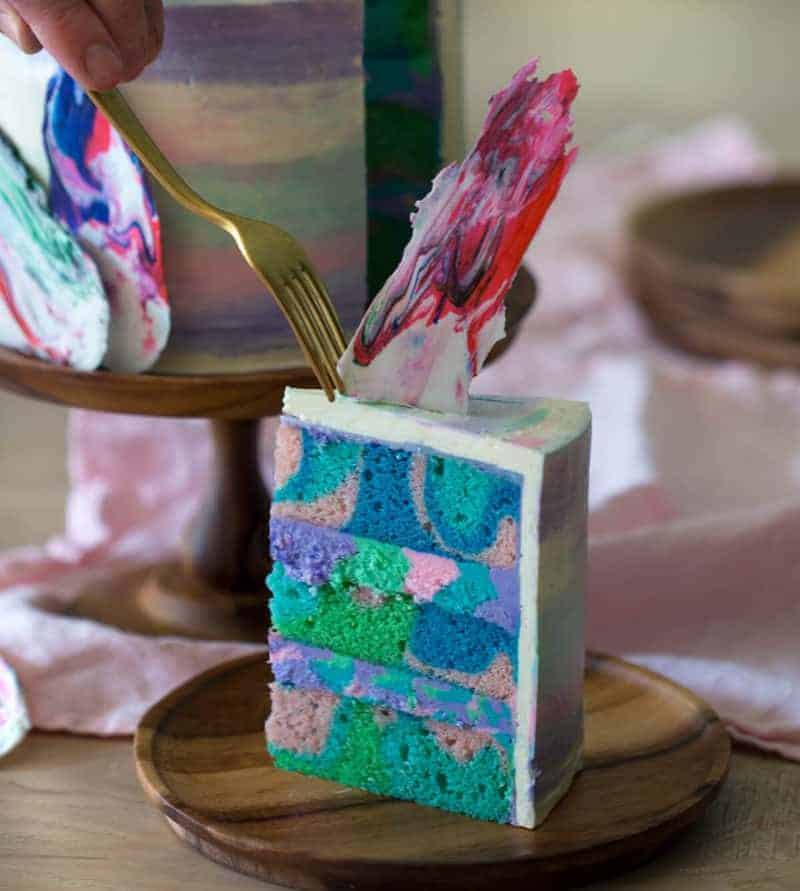 a photo of a rainbow swirl cake piece on a wooden plate