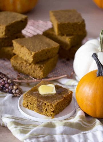 A piece of pumpkin cornbread on a plate next to several pumpkins