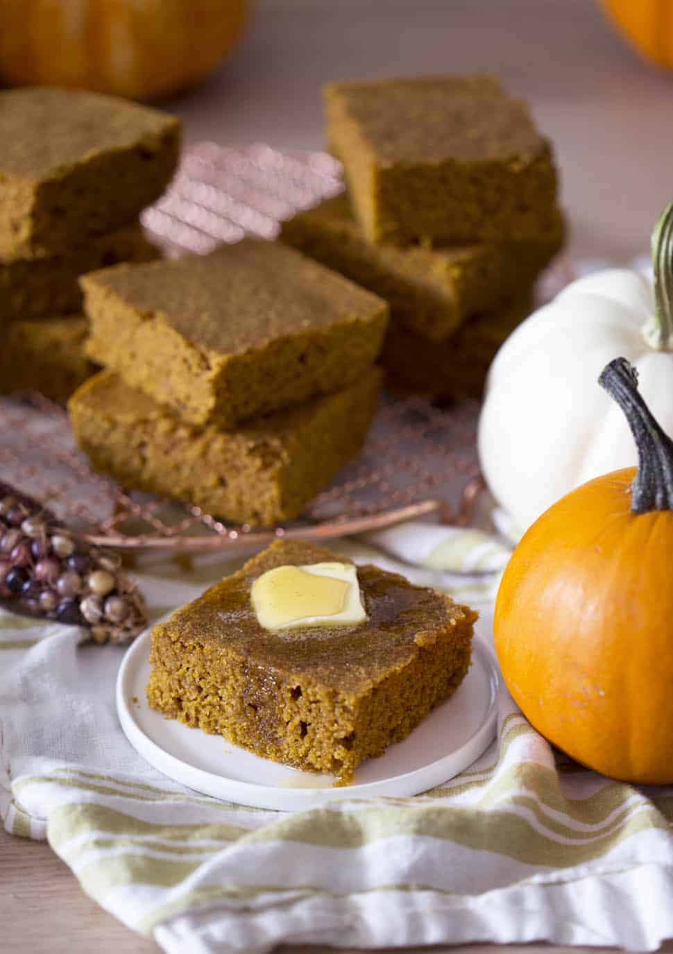 A piece of pumpkin cornbread on a plate next to several pumpkins