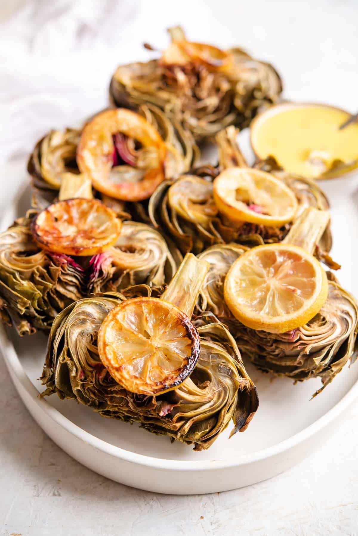 A side shot of roasted artichokes on a serving plate