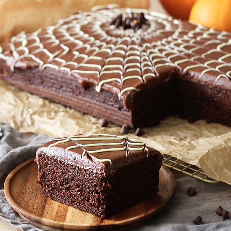 a photo of a spider web sheet cake with a bpiece in teh foreground on a wooden plate.