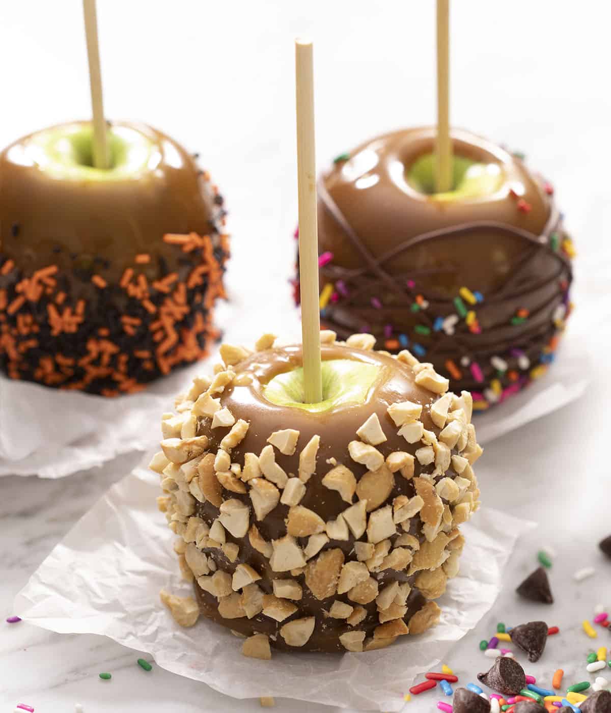 Three caramel apples with different toppings from nuts to sprinkles.