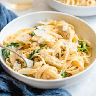 A bowl of spinach artichoke pasta with a fork.