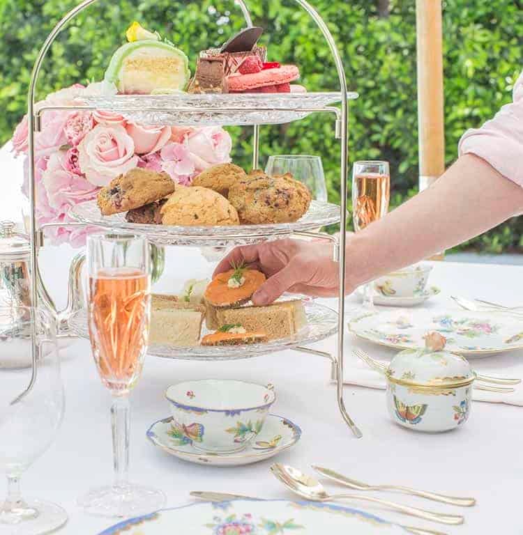 Tea sandwiches on a tiered tray among flowers and porcelain.