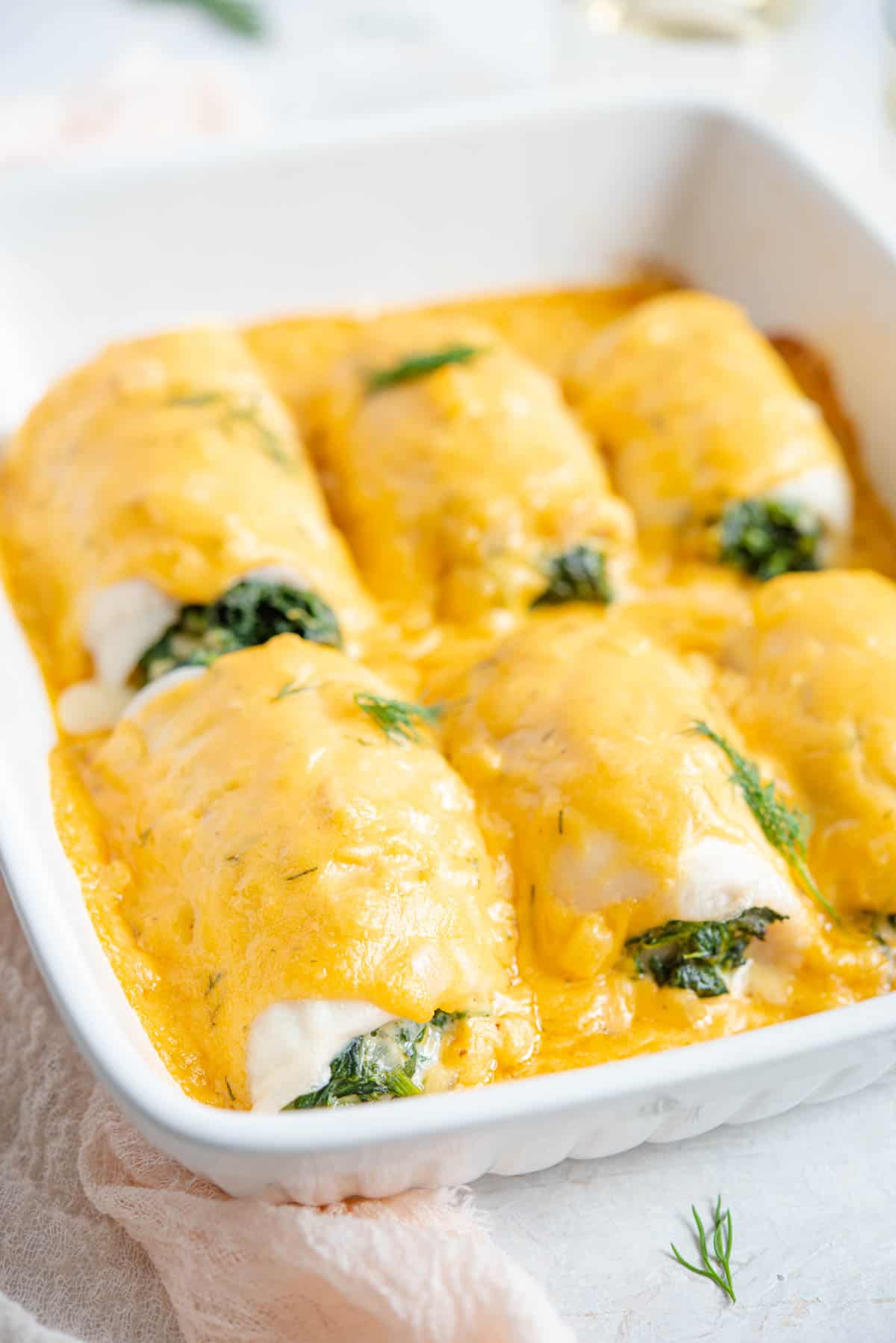 A side shot of baked fillet of sole in a baking dish with a cheesy sauce on top