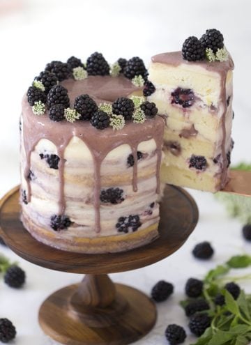 A slice of blackberry lemon cake being lifted from a cake stand.