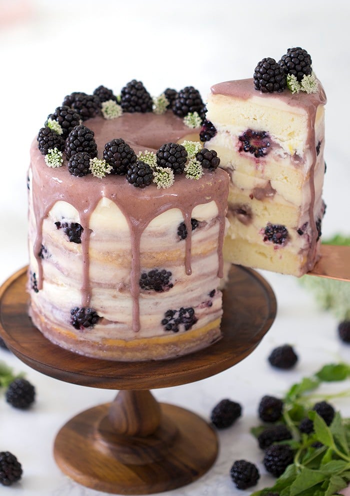 A slice of blackberry lemon cake being lifted from a cake stand.