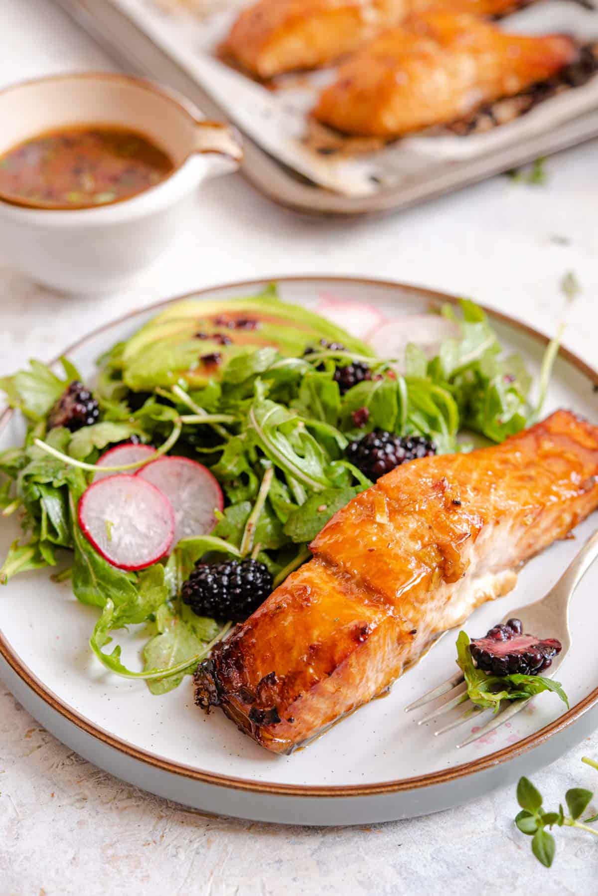 A side shot of glazed salmon on a modern plate with a blackberry salad