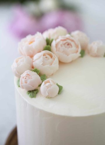 Close up 3/4 view of a lemon elderflower cake topped with soft pink buttercream peonies