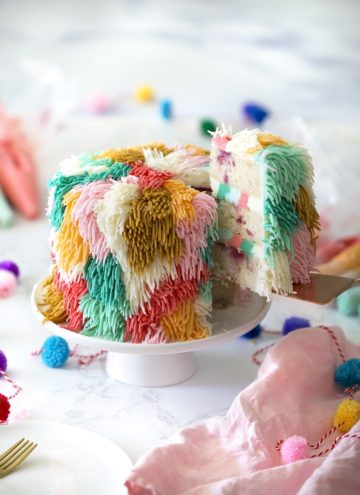 Photo of a colorful shag cake on a white cake stand with a piece being removed