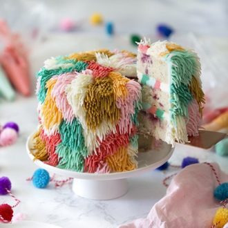 Photo of a shag cake on a white cake stand with a piece being removed