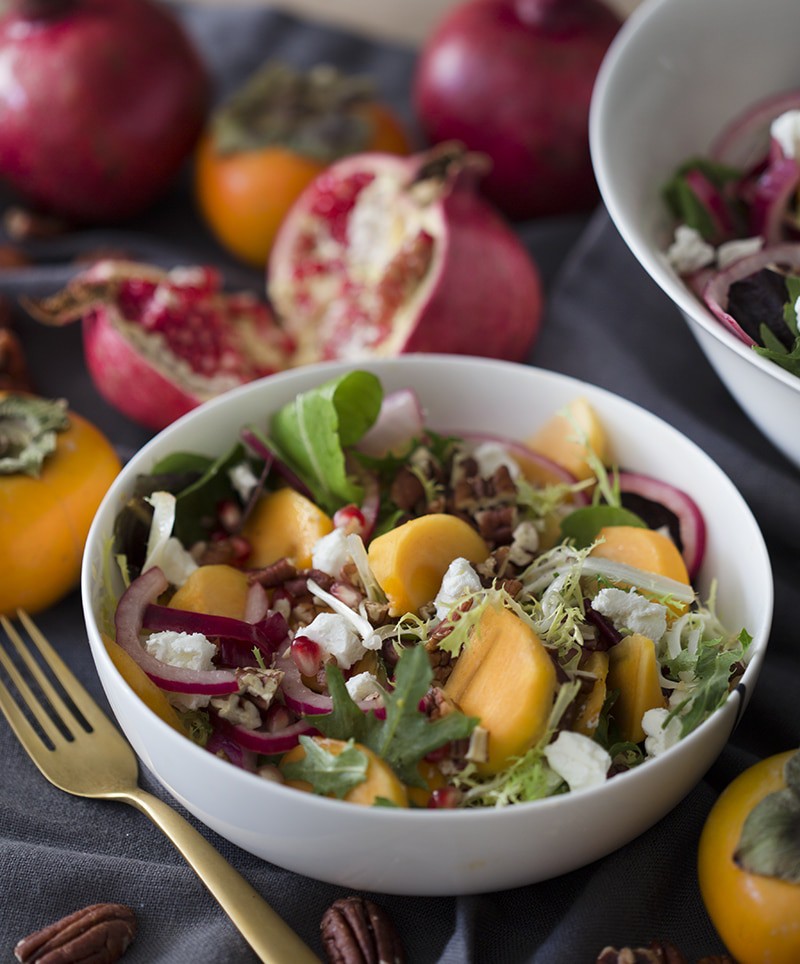 Photo of a persimmon sapad arranged in a bowl surrounded by pomegranates and persimmons
