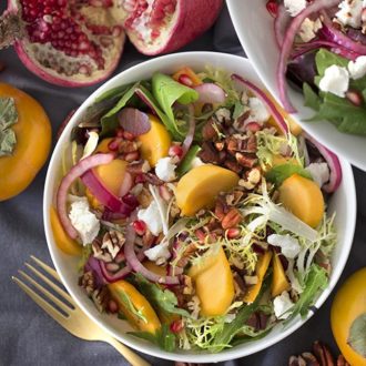 Photo of a persimmon salad with pomegranate seeds and pecans in a white bowl