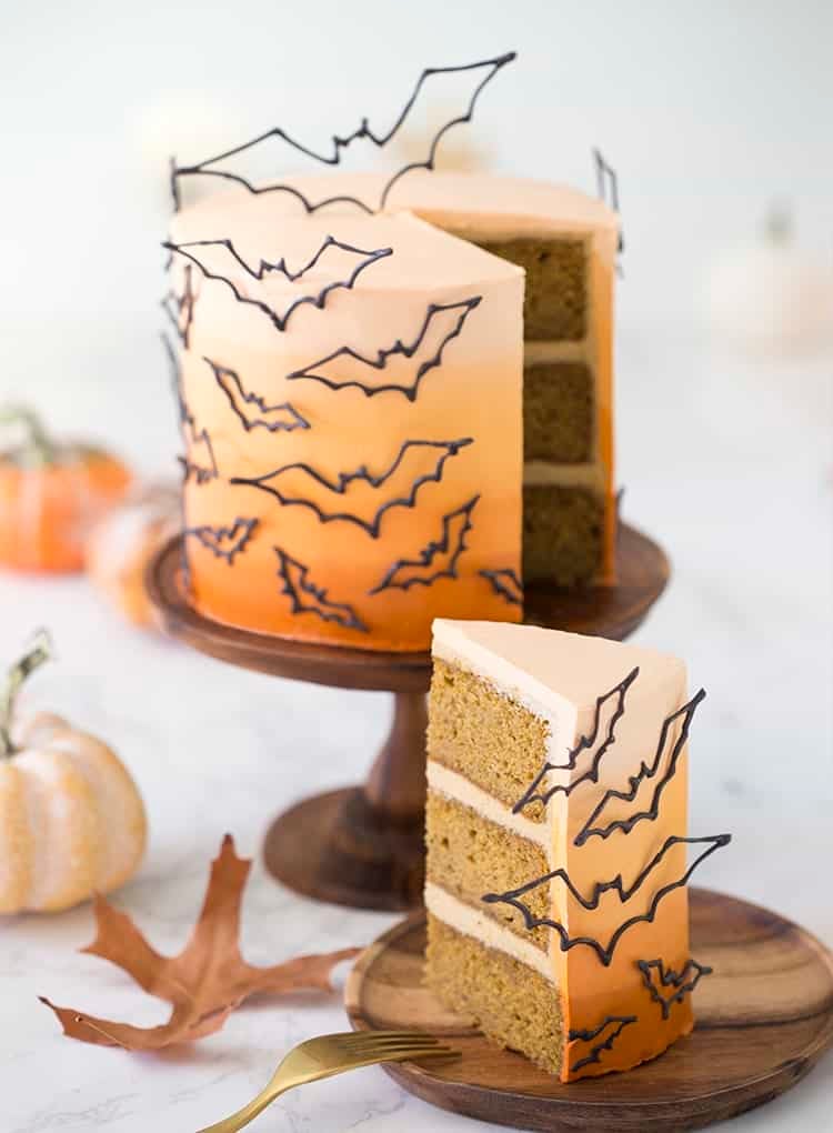photo of an ombre orange cake covered in candy melt bats on a wooden cake stand with a piece in the foreground