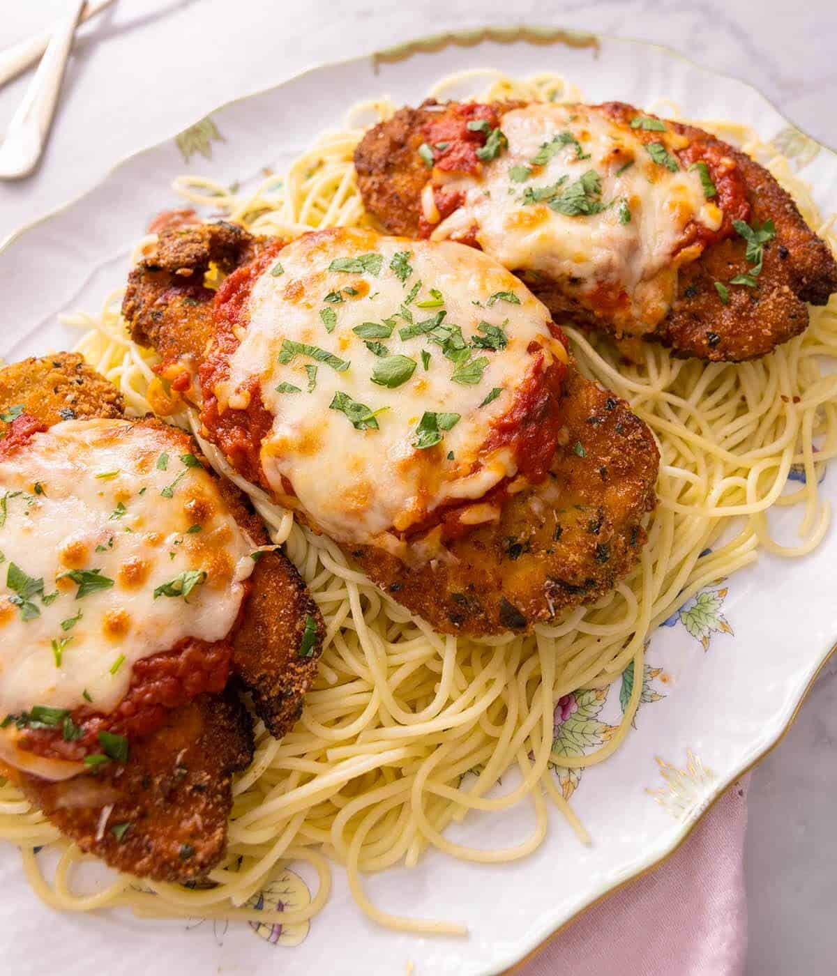 Three pieces of chicken parmesan on top of spaghetti. 