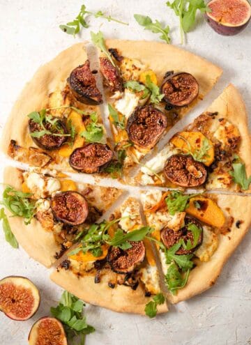 An overhead shot of a fig pizza cut into slices