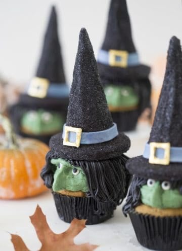 A photo of realistic looking witch cupcakes on a white table.