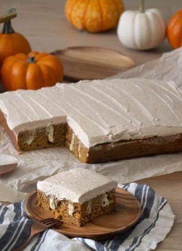 A pumpkin poke cake covered in brown butter frosting with a pice in the foreground.