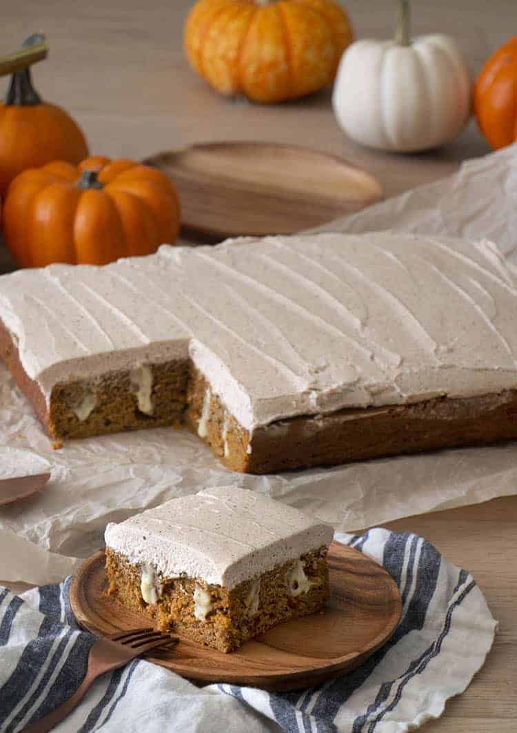A pumpkin poke cake covered in brown butter frosting with a pice in the foreground.