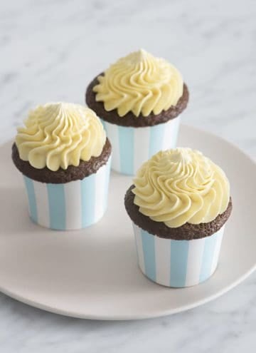 A photo of three chocolate cupcakes topped with dollops of french buttercream.