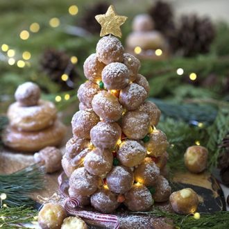 A photo of a croquembouche surrounded by evergreen cuttings and mini lights