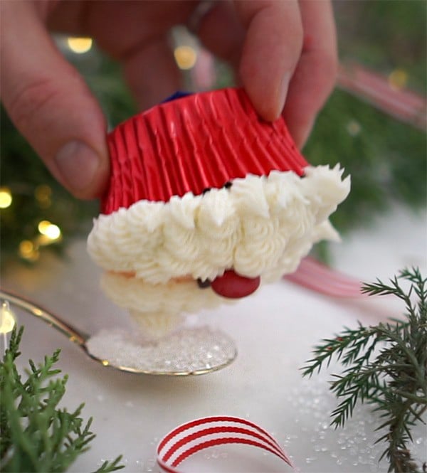 A photo of a Santa cupcake being dipped in sanding sugar