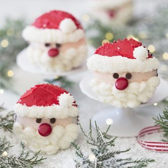A photo showing a group of Santa cupcakes on a white marble table with greenery.